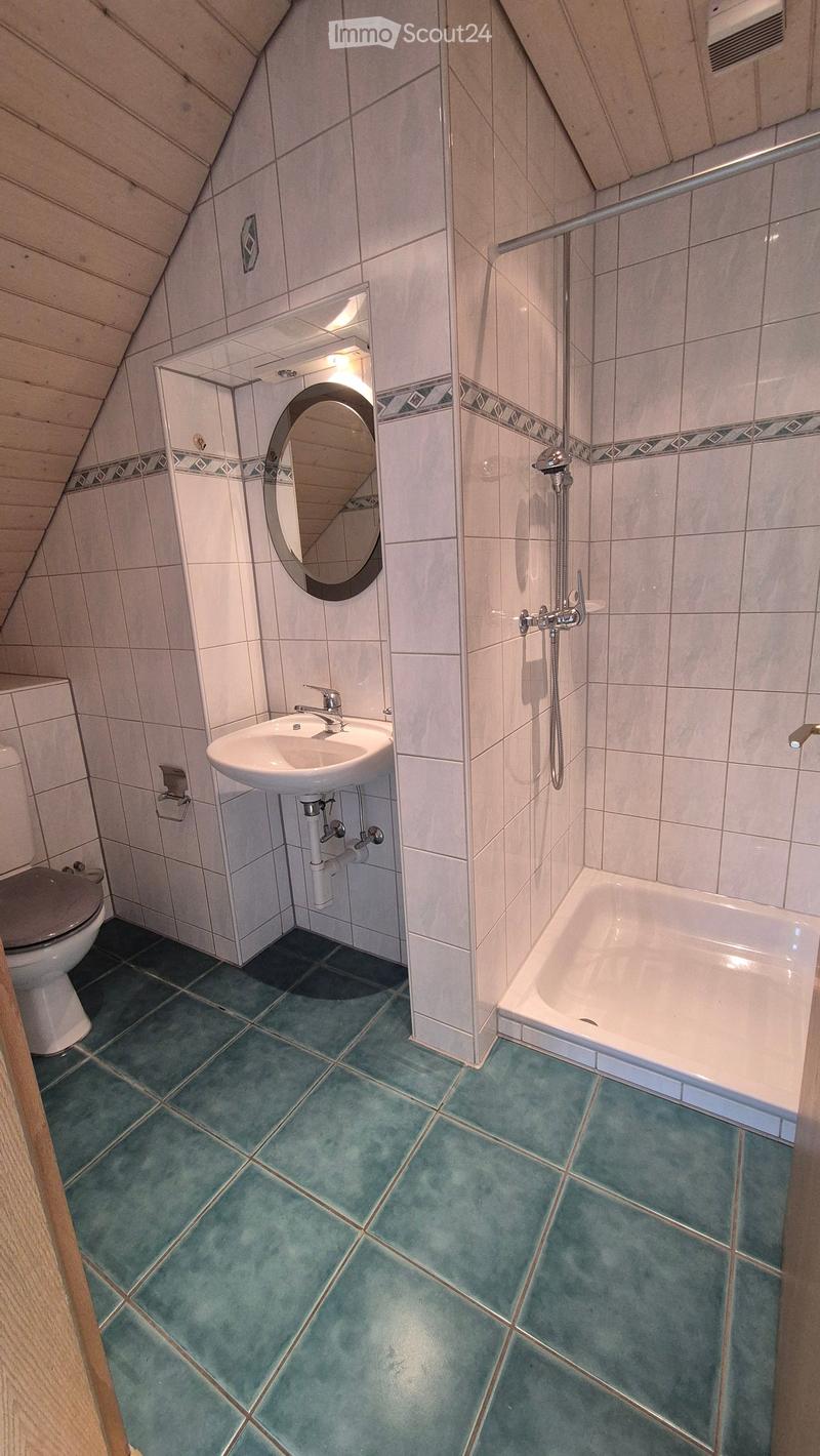 Bathroom with a toilet, sink, bathtub, and a round mirror. The walls are tiled with white tiles and decorative borders, and the floor is covered with blue tiles.