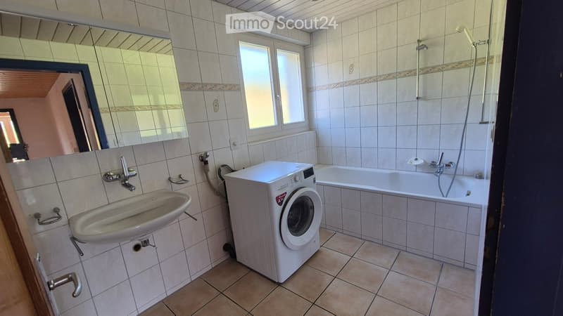 Bathroom with tiled walls and floor, featuring a sink, bathtub, washing machine, and large mirror.
