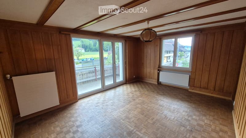 Empty room with wooden walls, herringbone wooden flooring, large windows, and a sliding glass door leading to a balcony.