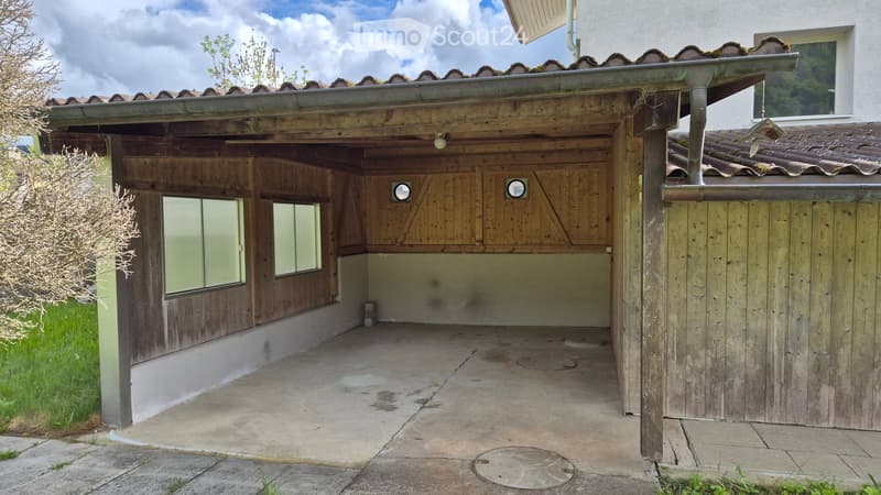Wooden garage with a covered entrance, concrete floor, and small windows on the side.