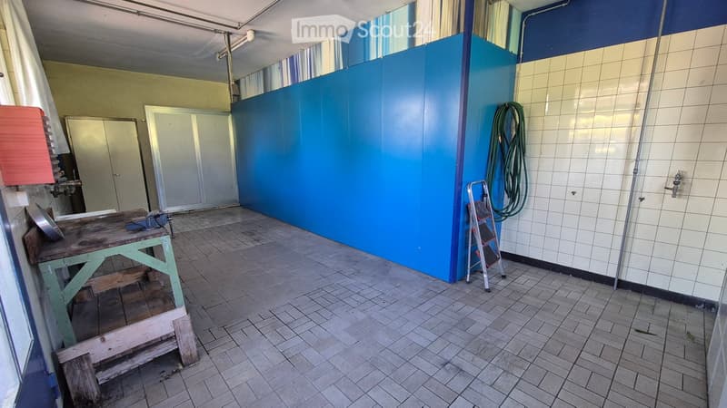 Empty room with tiled floor, blue wall, white tiled wall, wooden workbench, ladder, and coiled hose.