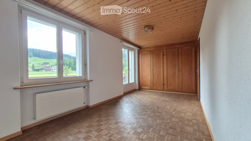 Empty room with wooden flooring, large windows offering a scenic view, wooden built-in closet, and a radiator under the windows.