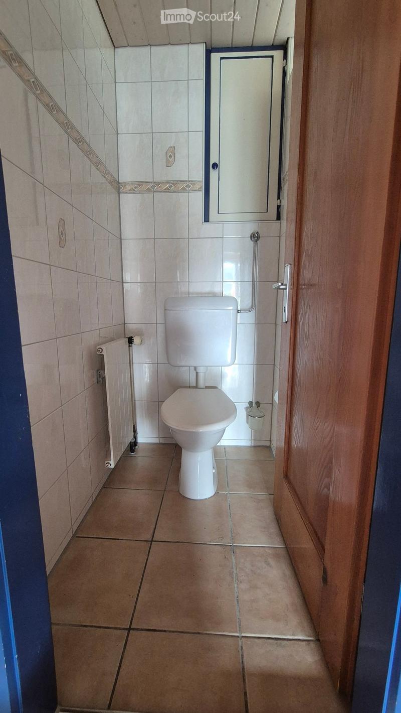 Small bathroom with beige tiled walls and floor, white toilet, radiator, mirror, and toilet paper holder.