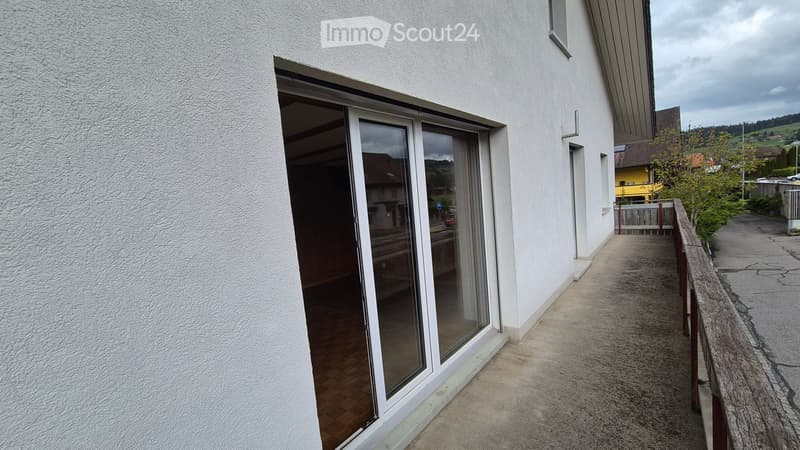 Balcony with wooden flooring, white railing, and a large sliding glass door leading to an interior space.