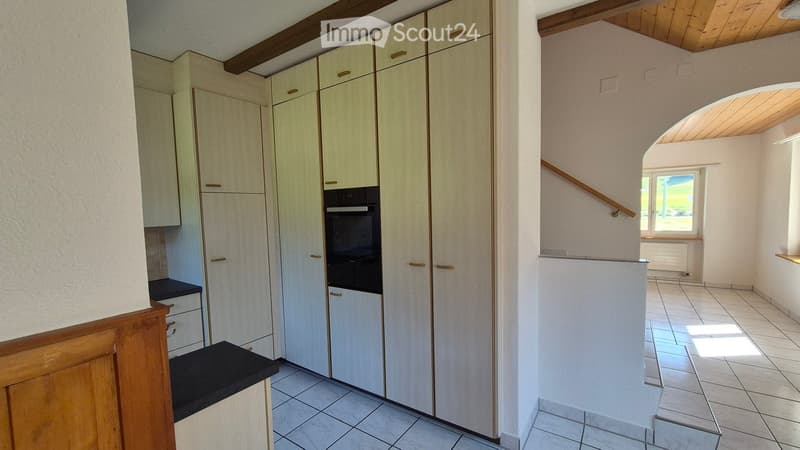 Empty kitchen and hallway area with light wooden cabinets, tiled flooring, and a window letting in natural light.
