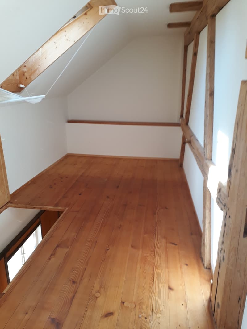 Empty hallway with wooden flooring and white walls, featuring exposed wooden beams and a slanted ceiling typical of an attic space.