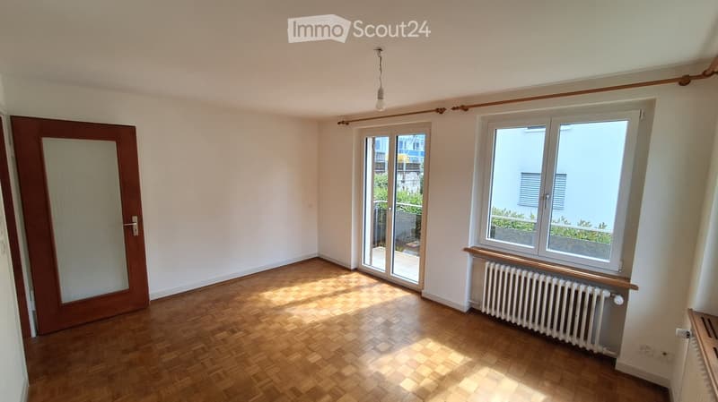 Empty room with wooden flooring, white walls, large windows, and a sliding glass door leading to a balcony.