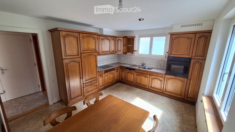 Bright kitchen with wooden cabinets, a sink, an oven, and a small dining area with a table and chairs.
