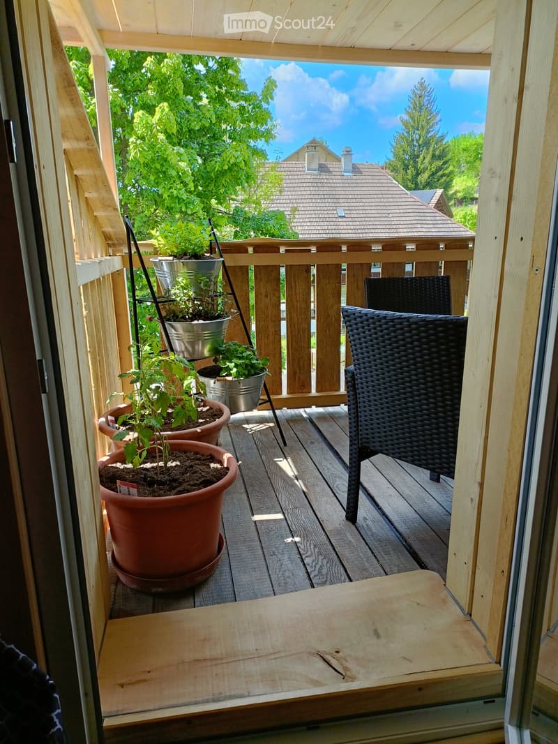 Balcony with wooden decking, potted plants, a wicker chair, and a small table.
