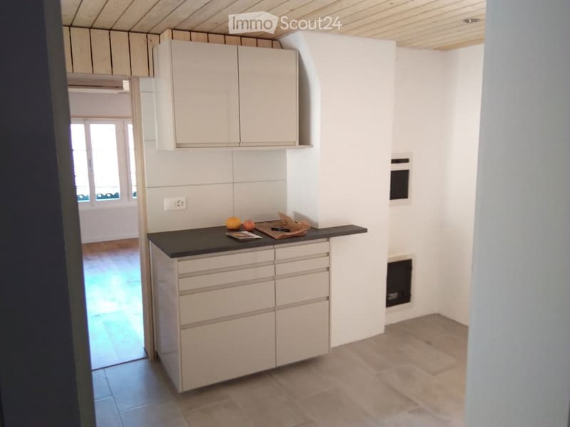 Modern kitchen with white cabinets, black countertop, and built-in oven. Countertop has fruits and a magazine.