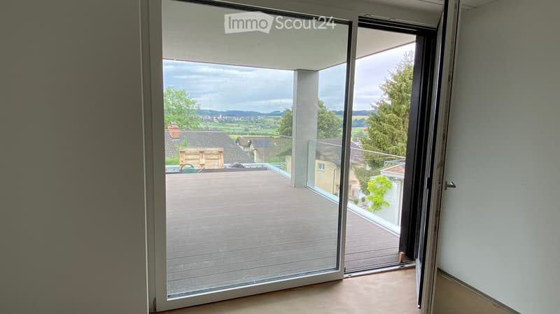 View of a modern balcony with glass sliding doors, wooden decking, and scenic countryside view.