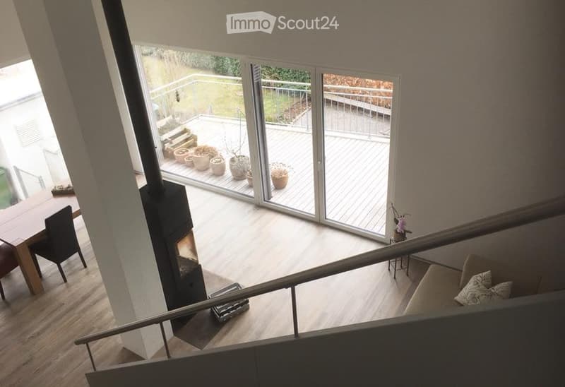Modern open-plan living and dining area with a fireplace, large windows leading to a balcony, and a staircase leading to an upper level.
