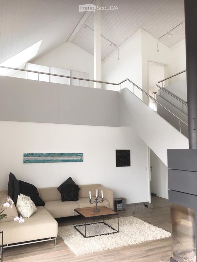 Modern living room with a fireplace, white walls, wooden flooring, a beige sectional sofa, a glass coffee table, and a white shag rug.