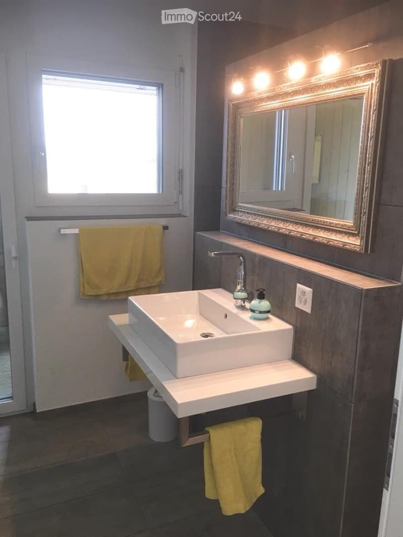 Modern bathroom with a white sink, large mirror with LED lighting, and yellow towels.
