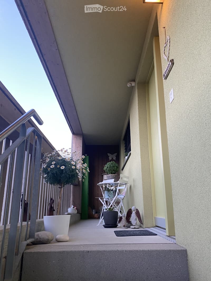 Balcony with a small table, chair, potted plants, and decorative items.