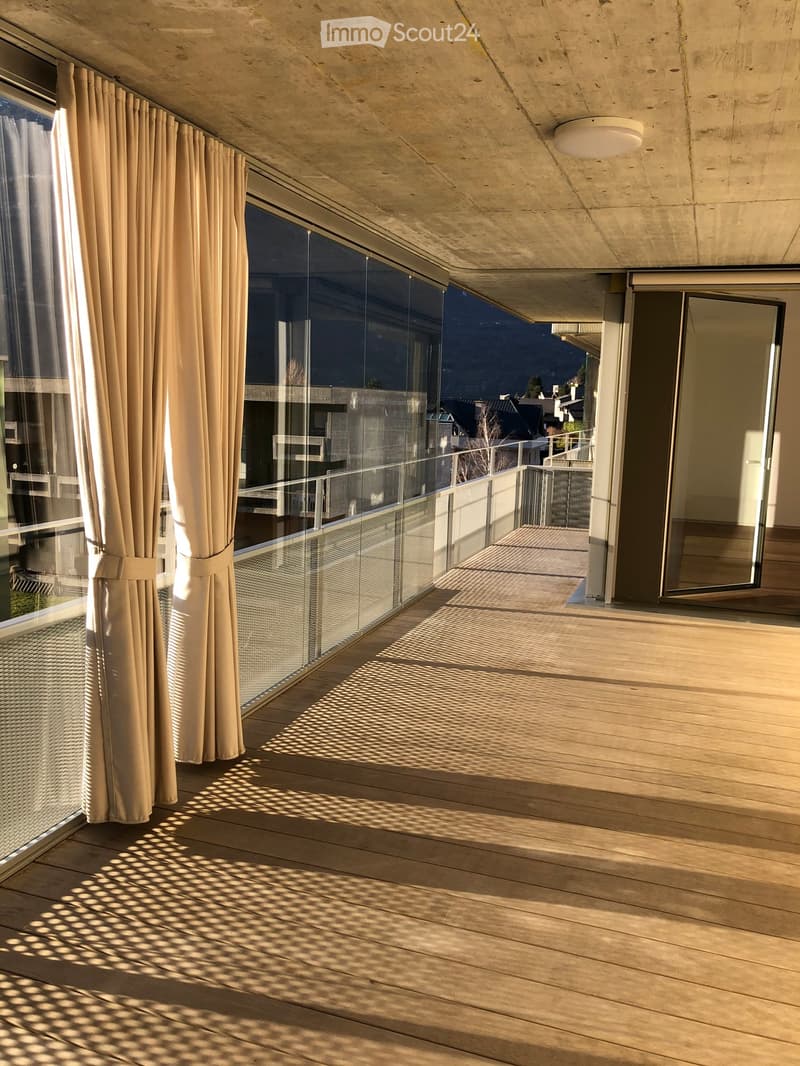 Modern balcony with wooden decking, large glass windows, and a view of the cityscape.