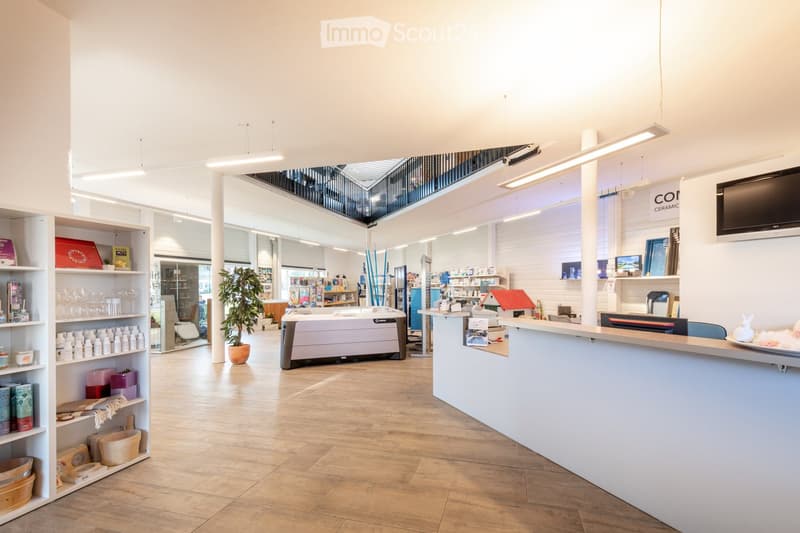 Bright, modern retail space with wooden flooring, white walls, shelves filled with products, a counter, a screen, a hot tub, and a potted plant.