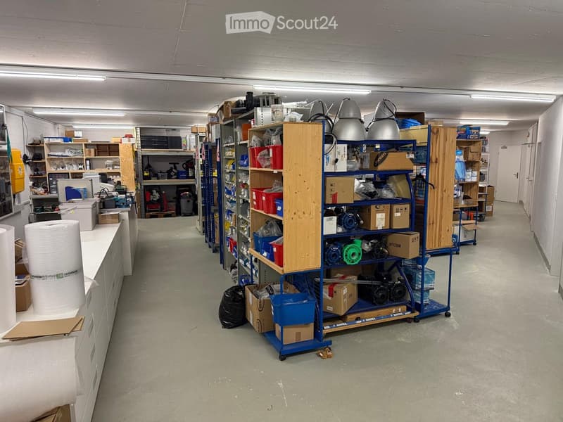 A long, well-lit storage corridor with metal shelving units, various tools, equipment, and storage boxes neatly arranged along both sides.