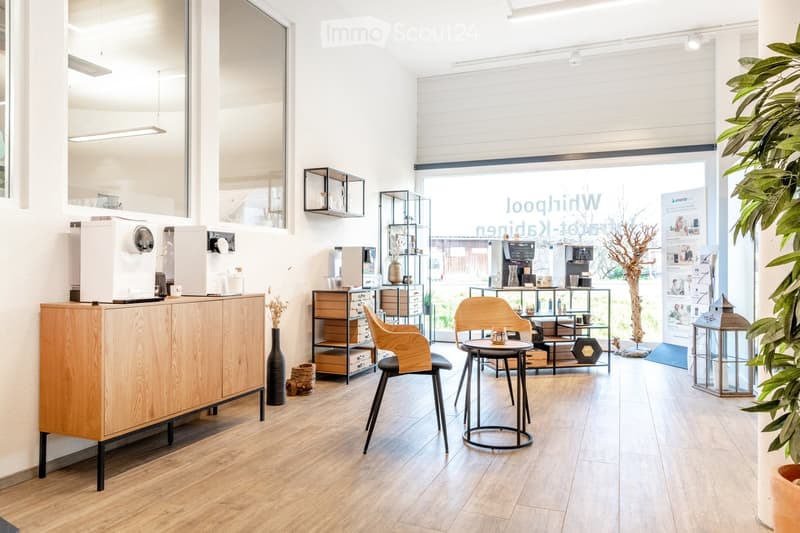 Bright, modern room with wooden flooring, large windows, and a mix of contemporary furniture including a wooden cabinet, chairs, a small round table, shelves, and decorative vases.