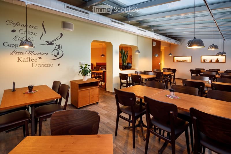Wooden tables and chairs, wooden floor, wall with coffee-themed wall art, hanging lamps, potted plants, wooden cabinet with a plant on top