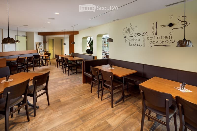 Wooden floor, wooden tables and chairs, long benches, hanging lamps, wall with text, potted plant