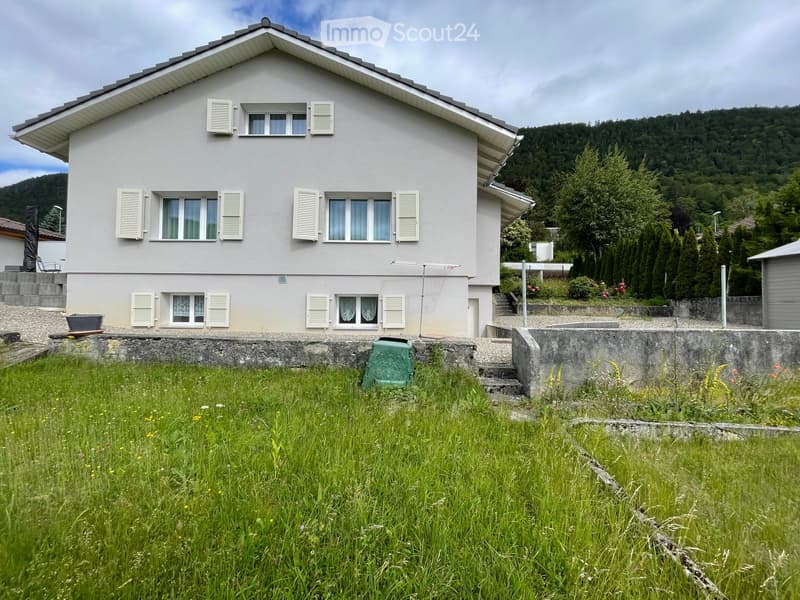 Two-story house with white exterior, multiple windows with shutters, and a well-maintained garden in front.