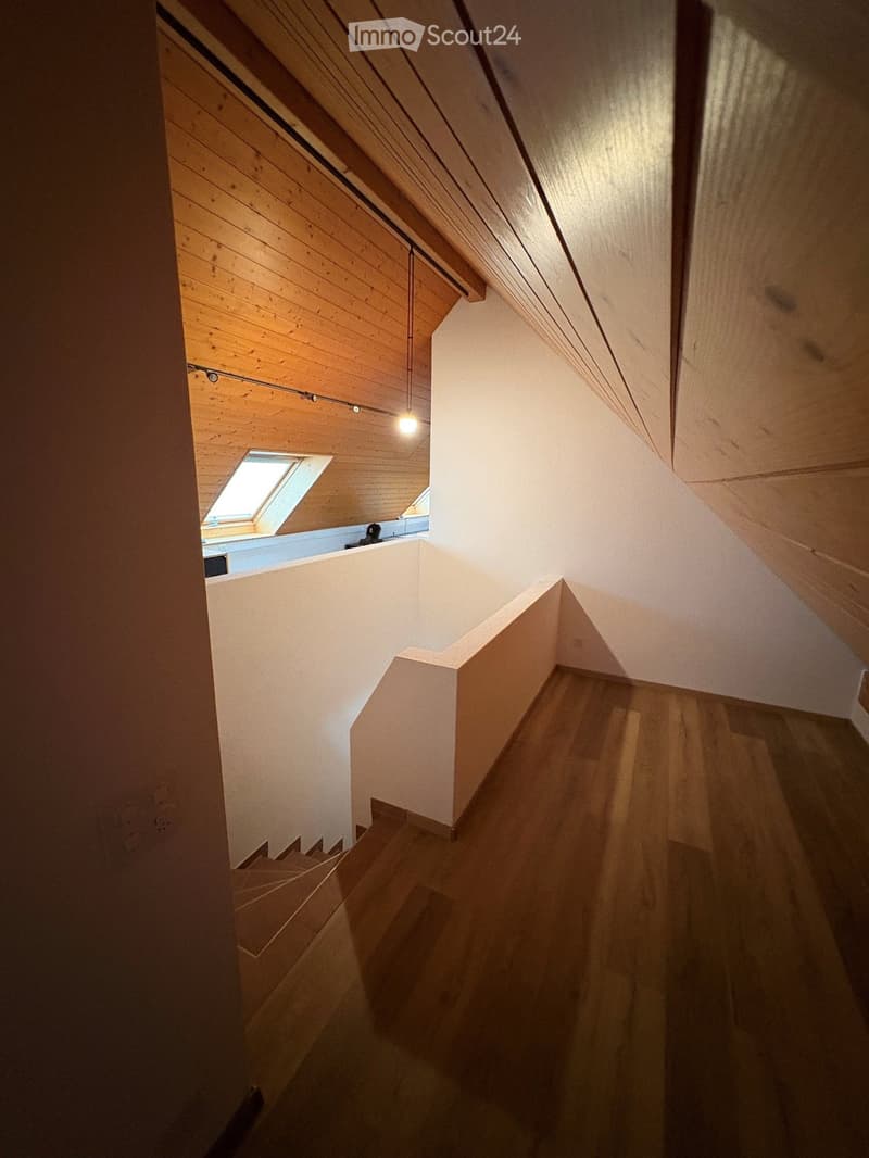 Spacious hallway with wooden flooring, white walls, and a wooden ceiling. Features a staircase leading upwards and a skylight window at the top of the stairs.