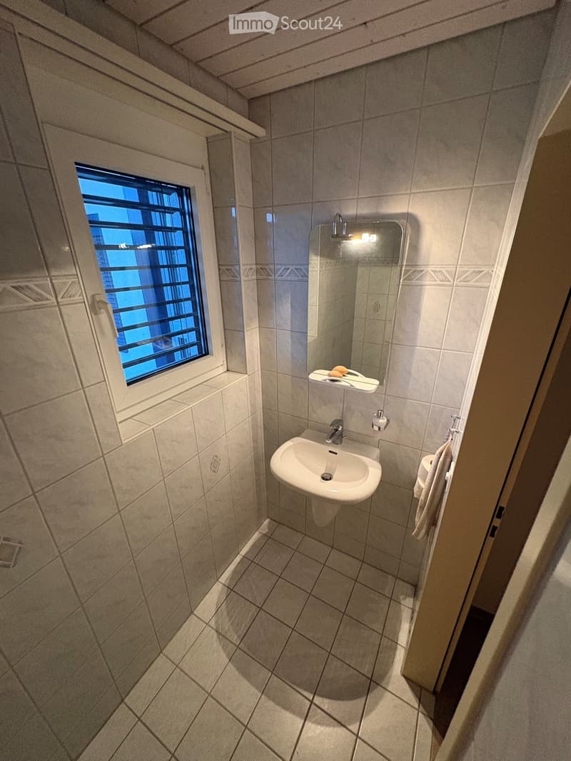 Small bathroom with tiled walls and floor, featuring a sink, mirror, and window with bars.