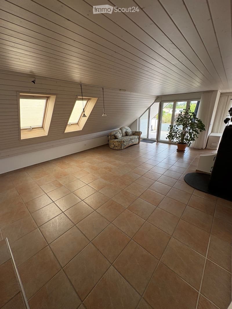 Loft-style room with wooden slat ceiling, tiled floor, large windows, and a small sofa near the windows.