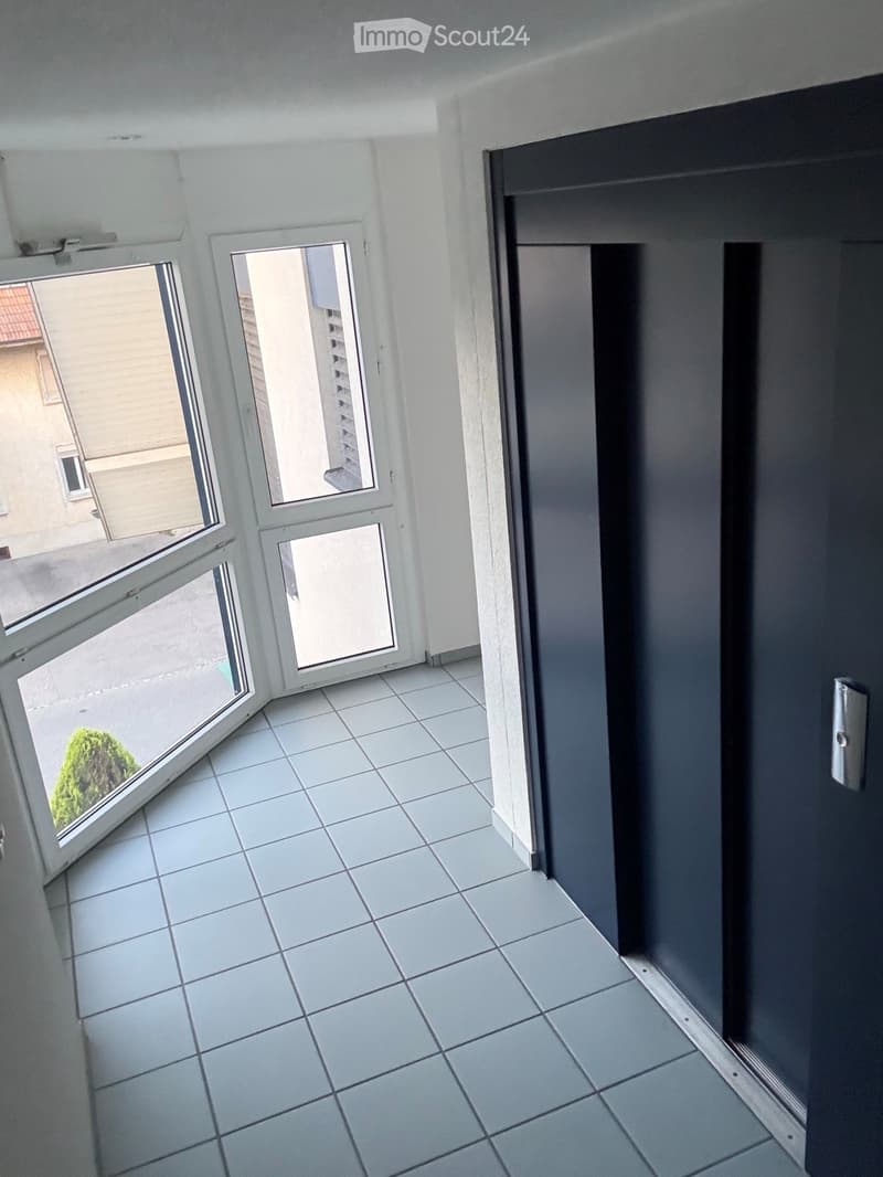 Empty room with tiled floor, white walls, and large windows with open blinds, leading to a view of the outside.