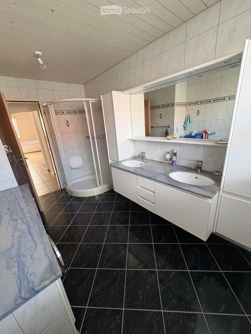 Modern bathroom with black tiled floor, white cabinets, double sink, mirror, and a glass-enclosed shower. The space features sleek fixtures and a clean, contemporary design.