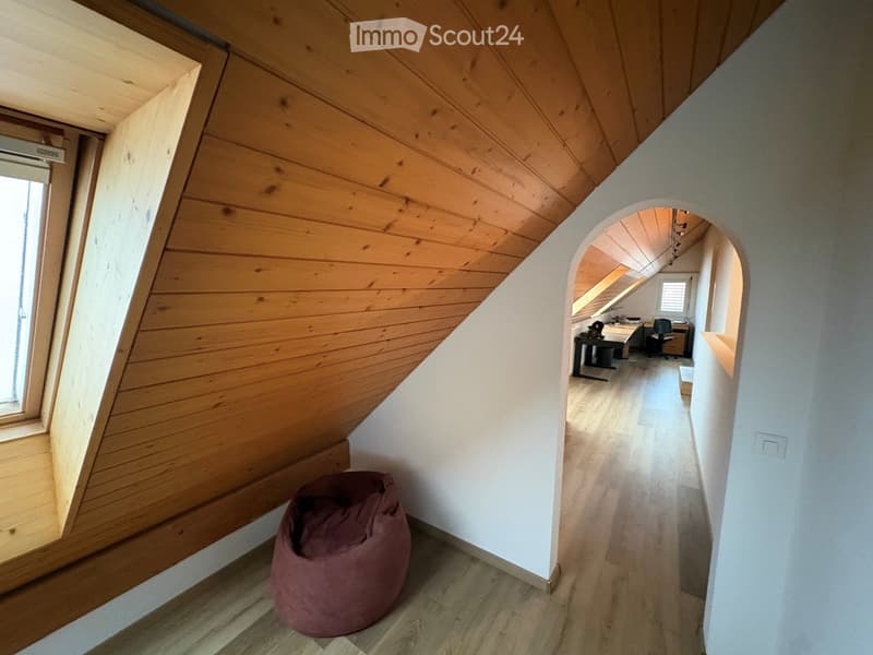 Loft-style room with wooden walls and ceiling, featuring a bean bag chair and an adjacent workspace with a desk and chair.