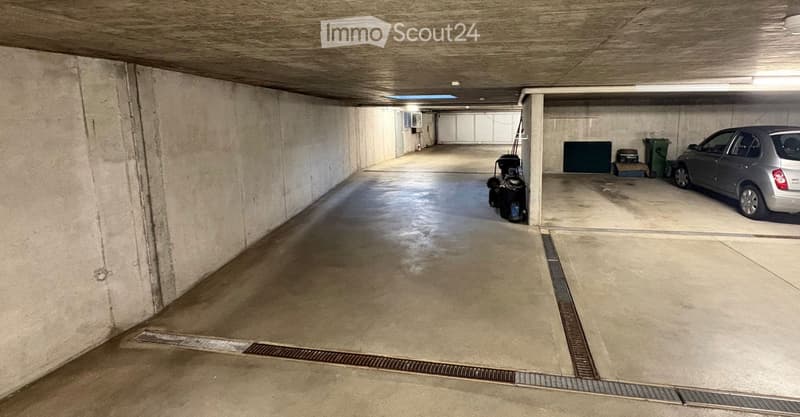 Underground parking area with concrete floors and walls, a parked car, and a trash bin.
