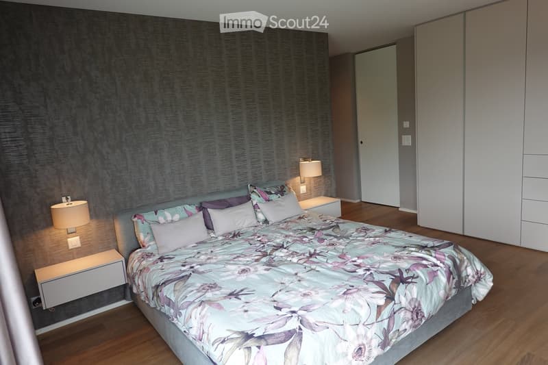 Modern bedroom with a large bed, floral duvet, nightstands, lamps, and a wardrobe.