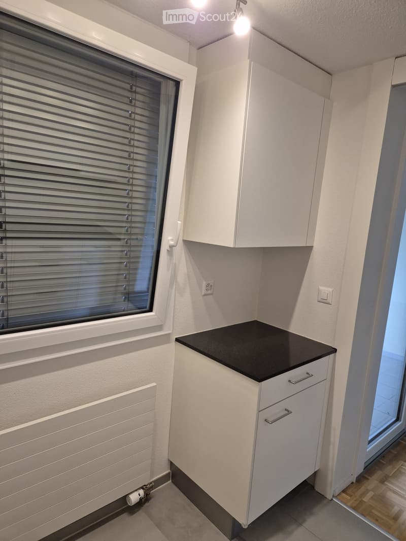 Modern kitchen with white cabinets, black countertop, and a window with blinds.