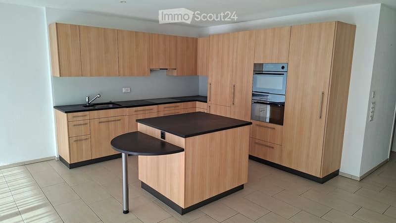 Modern kitchen with light wood cabinets, black countertops, a central island, and built-in oven.
