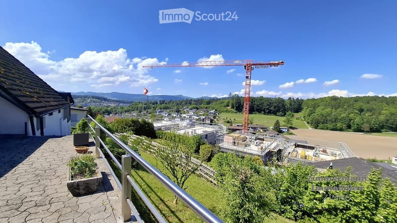 Balcony overlooking a town with a construction site, a crane, and surrounding greenery.