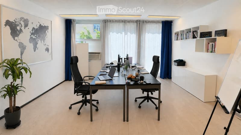 Modern office space with a large desk, two ergonomic chairs, multiple laptops, screens, books, and a potted plant. Shelves with books and decorative items are visible.