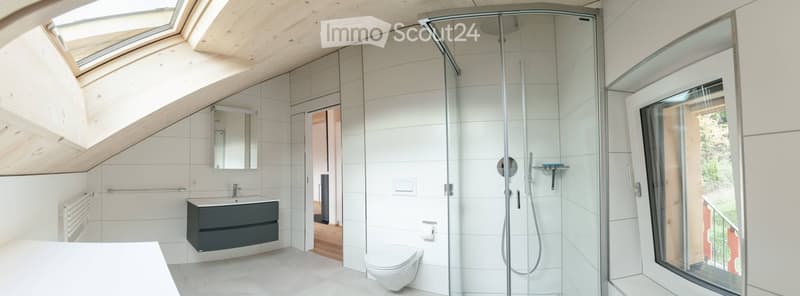 Modern bathroom with white tiles, a glass-enclosed shower, a sink with a dark cabinet, a toilet, and a large window offering a view of the garden.