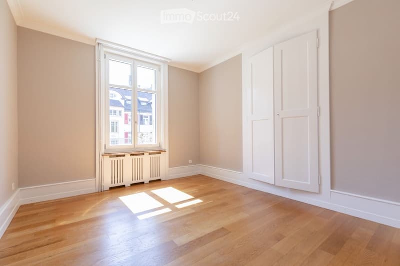 Empty room with wooden flooring, large window, radiator, and white walls.