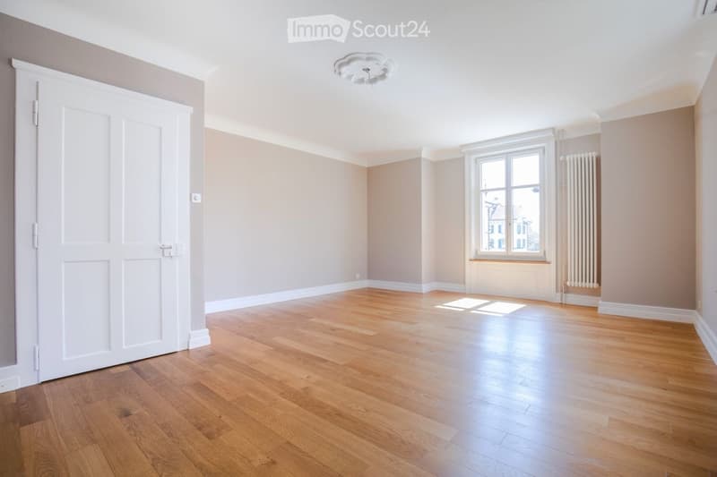 Empty room with wooden flooring, white walls, large window, and white door.