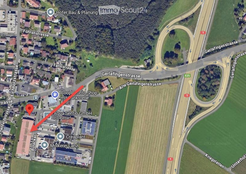 Aerial view of a residential area with a road intersection and surrounding farmland and greenery. The highlighted property is marked with a red arrow.