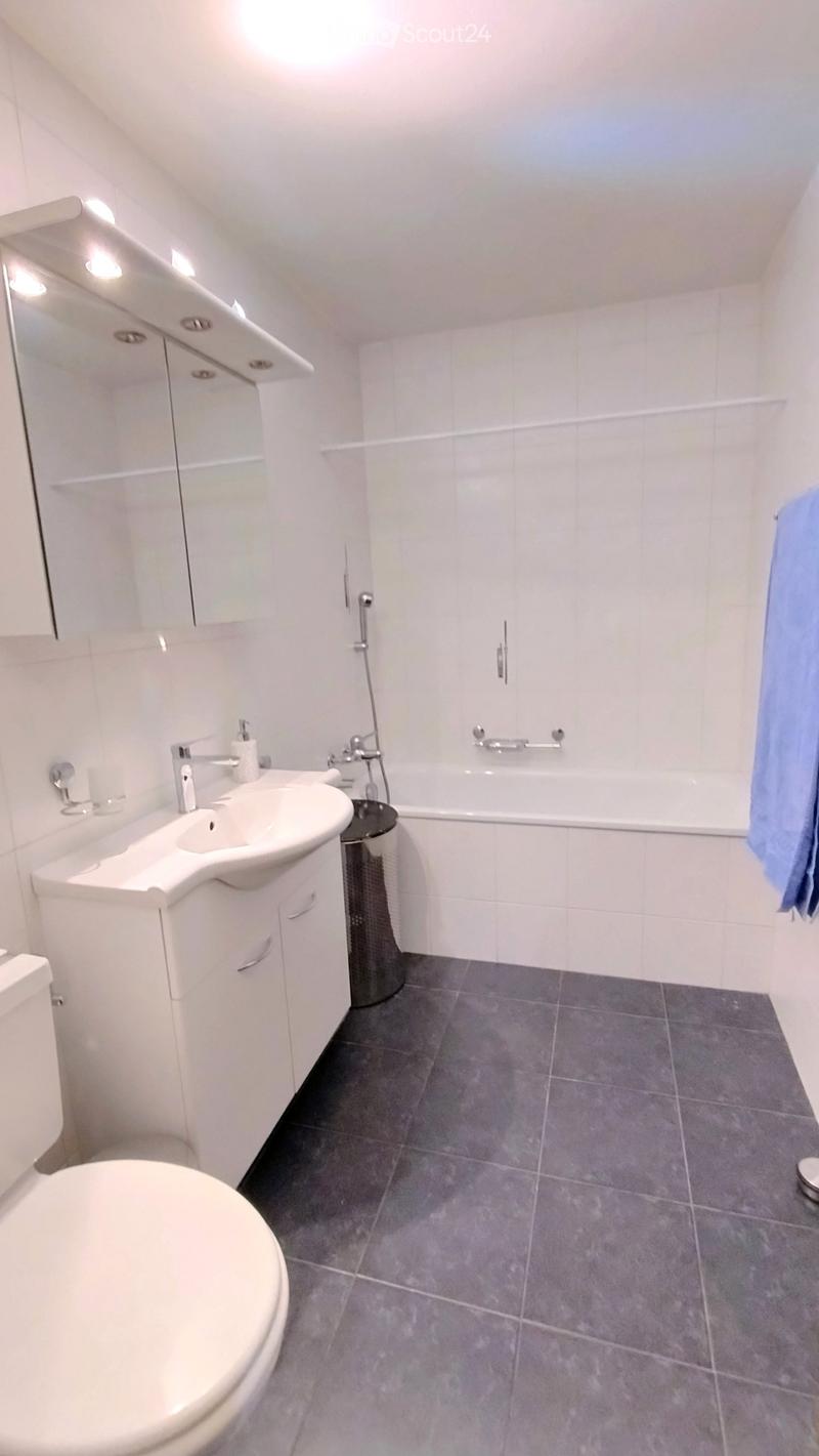 Modern bathroom with white tiles, a toilet, a sink with a mirror, a bathtub, and a towel hanging on the wall.