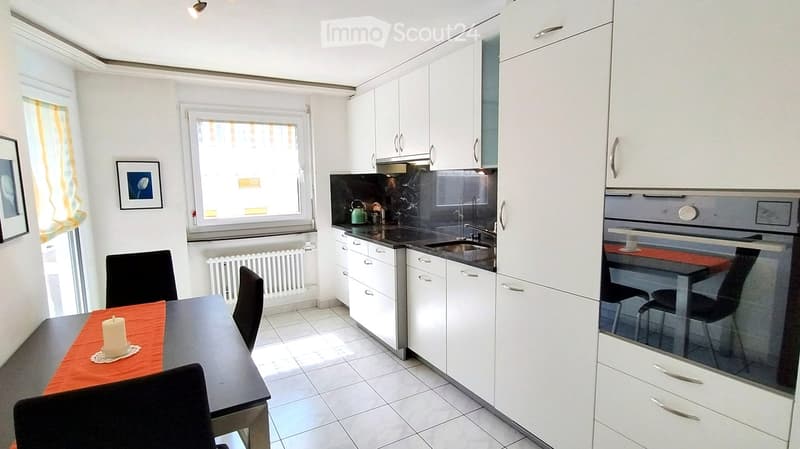 Modern kitchen with white cabinets, black countertops, stainless steel sink, and a small dining area with a table and chairs.