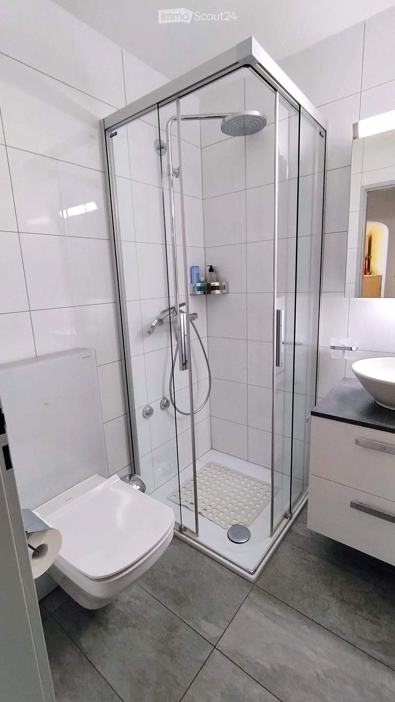 Modern bathroom with white tiles, a glass-enclosed shower, toilet, sink, and mirror.