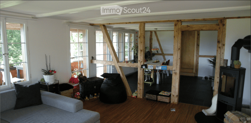 Living room with wooden floor, large windows, sofa, coffee table, fireplace, and a small table with chairs in the background.