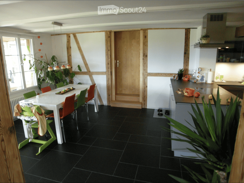 Modern kitchen and dining area with black tiled floor, white dining table, colorful chairs, kitchen island, and potted plants.