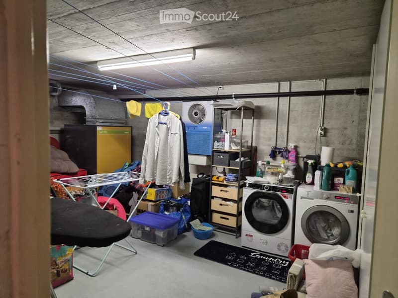 Laundry room with washing machine, dryer, ironing board, chair, shelf, fan, storage boxes, cleaning supplies, and clothing rack.