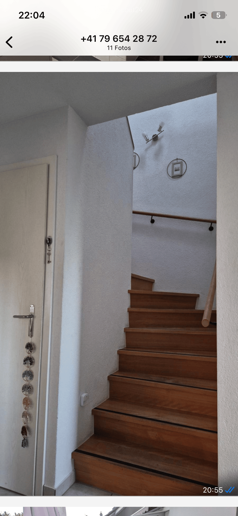 Wooden staircase with white walls, a door on the left, and a light fixture on the wall above the stairs.