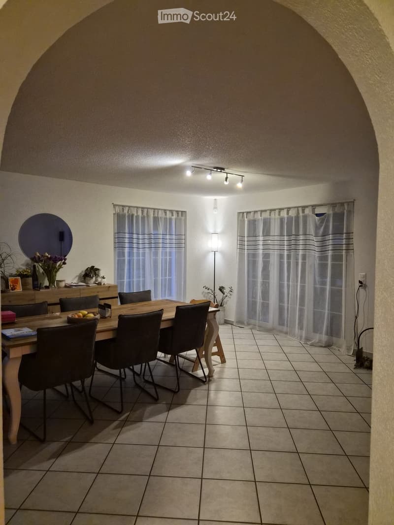 Dining room with a wooden dining table, six chairs, a mirror, and a small shelf with decorative items.